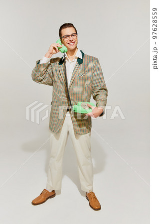 Portrait of young emotive man in retro style outfit posing with old-fashioned phone isolated over grey background. Concept of fashion, lifestyle, emotions. 97628559