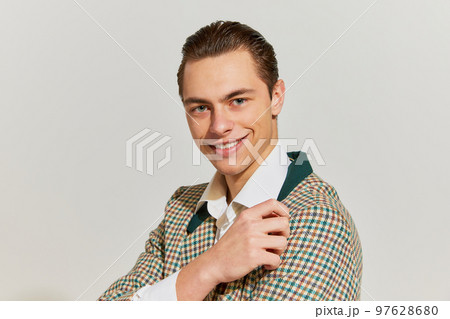 Half-length portrait of young handsome man in vintage old-fashioned jacket looking at camera with charming smile over grey background. Concept of retro fashion, style, emotions Half-length portrait of young handsome man in vintage old-fashioned jacket looking at camera with charming smile over grey background. Concept of retro fashion, style, emotions 97628680