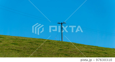 A power lines in a field. Minimalistic landscape, electric post on grass field, sky. 97630310