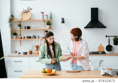 Two girlfriends cut fruit in the kitchen Two girlfriends cut fruit in the kitchen 97632673
