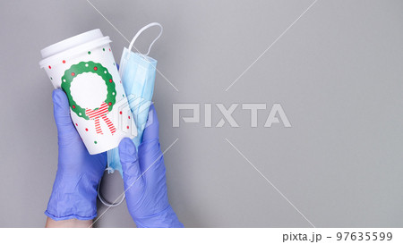 Hands in protective blue gloves with medical mask holds coffee paper cup on grey background with copy space. Virus protection. Nurse, doctor, barista, delivery service. Hands in protective blue gloves with medical mask holds coffee paper cup on grey background with copy space. Virus protection. Nurse, doctor, barista, delivery service. 97635599