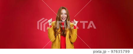 Hooray success. Portrait of happy cheerful and sincere cute ginger woman in yellow coat raising clenched fists and celebrating joyfully positive news, triumphing over win and smiling broadly Hooray success. Portrait of happy cheerful and sincere cute ginger woman in yellow coat raising clenched fists and celebrating joyfully positive news, triumphing over win and smiling broadly 97635799