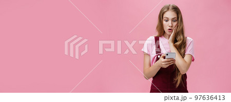 Girl found out shocking truth after reading message in smartphone pressing arm to cheek in surprise staring concerned and speechless at cellphone screen reacting to unexpected news over pink wall Girl found out shocking truth after reading message in smartphone pressing arm to cheek in surprise staring concerned and speechless at cellphone screen reacting to unexpected news over pink wall 97636413