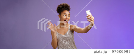Friendly stylish confident african-american woman in silver glittering dress waving raised palm hello hi gesture record video smartphone greeting internet followers blogging during party Friendly stylish confident african-american woman in silver glittering dress waving raised palm hello hi gesture record video smartphone greeting internet followers blogging during party 97636995