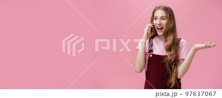 Portrait of popular outgoing and talkative young attractive girl in overalls waving raised hand during conversation talking on smartphone amused and excited gossiping with friend via cellphone Portrait of popular outgoing and talkative young attractive girl in overalls waving raised hand during conversation talking on smartphone amused and excited gossiping with friend via cellphone 97637067