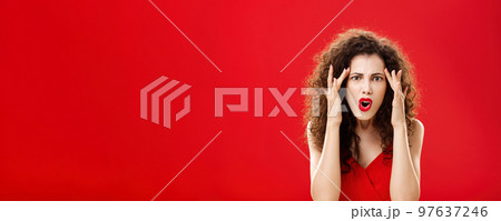 Woman cannot understand how dumb person should be. Pissed and annoyed displeased angry woman with curly hairstyle in red dress holding fingers on temples complaining on stupid people around her 97637246