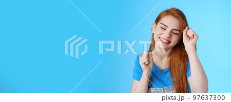 Close-up tender caring cute redhead 20s female tilt head, close eyes smiling dreamy, make winner dance, raise fist pumps celebration good news, stand optimistic good mood, blue background 97637300