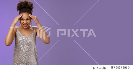 Pressured intense worried african-american woman in silver glittering dress grimacing cringing painful headache hold hand forehead suffer pain migraine, standing bothered blue background Pressured intense worried african-american woman in silver glittering dress grimacing cringing painful headache hold hand forehead suffer pain migraine, standing bothered blue background 97637669