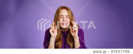Hopeful and dreamy cute tender redhead 20s girl in purple sweater making wish faithfully close eyes and cross fingers for good luck as anticipating miracle happen, supplicating over violet wall Hopeful and dreamy cute tender redhead 20s girl in purple sweater making wish faithfully close eyes and cross fingers for good luck as anticipating miracle happen, supplicating over violet wall 97637706