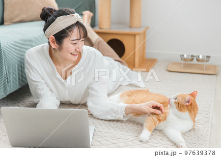 家で猫と一緒にパソコンを使う飼い主のアジア人女性（テレワーク・リモートワーク） 97639378