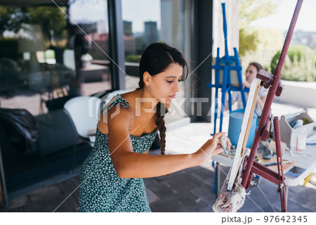 Young woman artist paints with a spatula on the canvas 97642345
