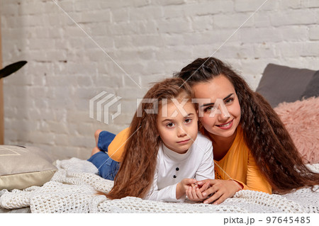 Love of young mother and daughter. They lie on the bed at home and have fun Love of young mother and daughter. They lie on the bed at home and have fun 97645485