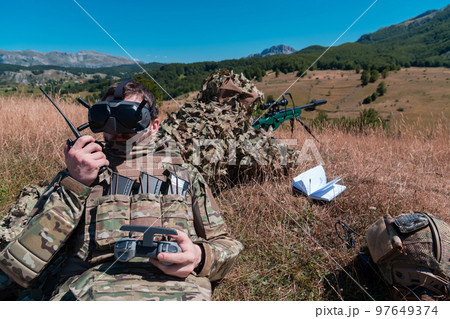 Sniper soldier assisted by an assistant to observe the area to be targeted with modern warfare tactical virtual reality goggles aerial drone military technology. 97649374