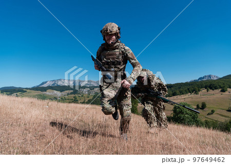 A sniper team squad of soldiers is going undercover. Sniper assistant and team leader walking and aiming in nature with yellow grass and blue sky. Tactical camouflage uniform. 97649462
