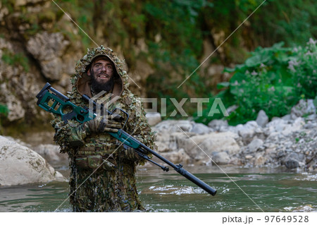 A military man or airsoft player in a camouflage suit sneaking the river and aims from a sniper rifle to the side or to target. A military man or airsoft player in a camouflage suit sneaking the river and aims from a sniper rifle to the side or to target. 97649528