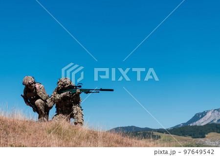 A sniper team squad of soldiers is going undercover. Sniper assistant and team leader walking and aiming in nature with yellow grass and blue sky. Tactical camouflage uniform. A sniper team squad of soldiers is going undercover. Sniper assistant and team leader walking and aiming in nature with yellow grass and blue sky. Tactical camouflage uniform. 97649542