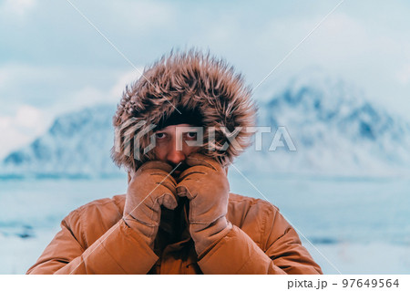 Headshot photo of a man in a cold snowy area wearing a thick brown winter jacket and gloves. Life in cold regions of the country. 97649564