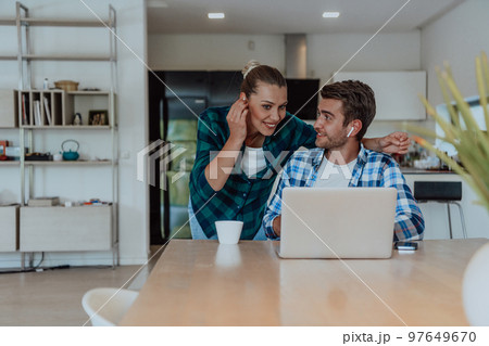 A young married couple is talking to parents, family and friends on a video call via a laptop while sitting in the living room of their modern house A young married couple is talking to parents, family and friends on a video call via a laptop while sitting in the living room of their modern house 97649670
