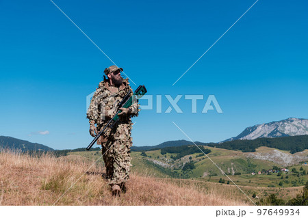 Army soldier holding a sniper rifle with scope and walking in the forest. war, army, technology and people concept. 97649934