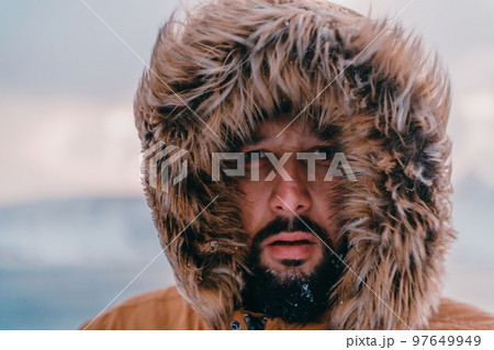 Headshot photo of a man in a cold snowy area wearing a thick brown winter jacket and gloves. Life in cold regions of the country. Headshot photo of a man in a cold snowy area wearing a thick brown winter jacket and gloves. Life in cold regions of the country. 97649949