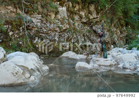 A military man or airsoft player in a camouflage suit sneaking the river and aims from a sniper rifle to the side or to target. A military man or airsoft player in a camouflage suit sneaking the river and aims from a sniper rifle to the side or to target. 97649992