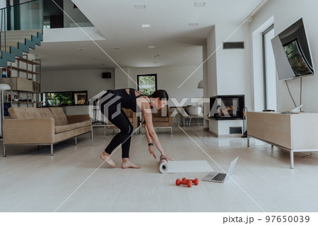 Young Beautiful Female Exercising, Stretching and Practising Yoga with Trainer via Video Call Conference in Bright Sunny Loft Apartment. Healthy Lifestyle, Wellbeing and Mindfulness Concept. 97650039
