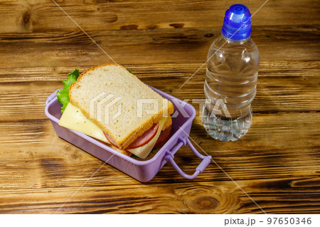 Lunch box with sandwiches and bottle of water on a wooden table Lunch box with sandwiches and bottle of water on a wooden table 97650346
