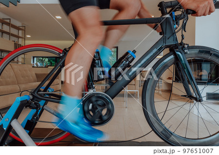 A man riding a triathlon bike on a machine simulation in a modern living room. Training during pandemic conditions. 97651007