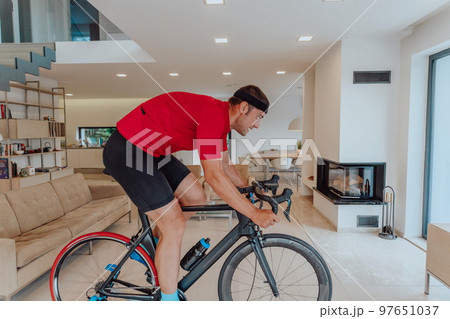 A man riding a triathlon bike on a machine simulation in a modern living room. Training during pandemic conditions. 97651037
