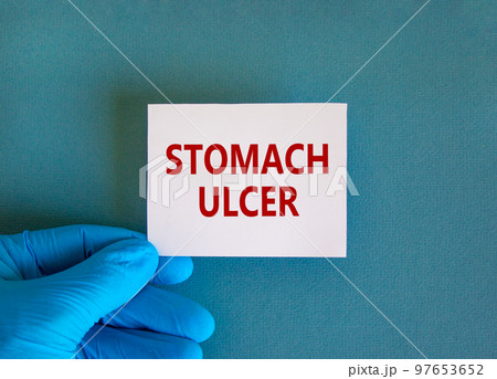 Medical and stomach ulcer symbol. Doctor hand. White card with words 'stomach ulcer'. Beautiful blue background. Doctor hand in blue glove. Medical and stomach ulcer concept. Copy space. 97653652