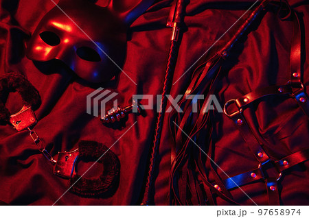Erotic sex toys for adults for BDSM sex with submission and domination. Handcuffs, mask and leather flogger whip on a black background Erotic sex toys for adults for BDSM sex with submission and domination. Handcuffs, mask and leather flogger whip on a black background 97658974