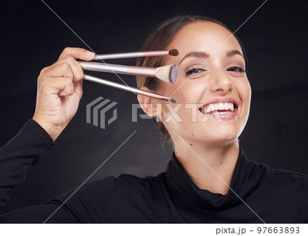 Makeup, brush or portrait of woman in studio with beauty cosmetics or facial foundation products on black background. Makeup artist, smile or happy girl brushes face for luxury skincare grooming Makeup, brush or portrait of woman in studio with beauty cosmetics or facial foundation products on black background. Makeup artist, smile or happy girl brushes face for luxury skincare grooming 97663893