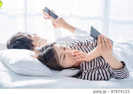 ベッドでスマホを見る夫婦 ベッドでスマホを見る夫婦 97674155