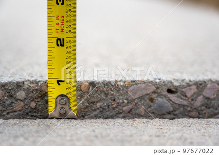 Frost heave crack in residential concrete sidewalk with tape measure  97677022