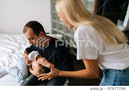 Close-up high-angle view of scared father and daughter hugging each other sitting on bed while aggressive mother angrily yelling at them at home. Angry wife scolding, raising voice, scream at family 97677290