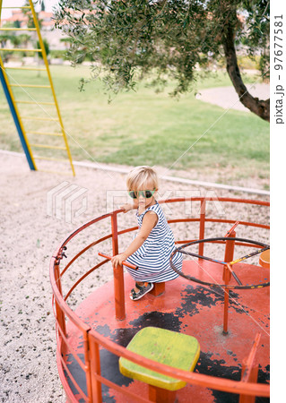 Little girl in sunglasses rides a spinning carousel on the playground. High quality photo 97677581