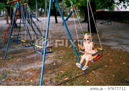 Little girl in sunglasses swings on a rope swing at the playground. High quality photo 97677712