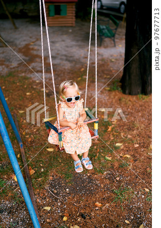 Little girl sits with her mouth open on a swing in the playground. High quality photo 97677713