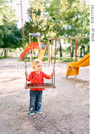 Little girl holding on to the handles of a wooden swing. High quality photo Little girl holding on to the handles of a wooden swing. High quality photo 97677792