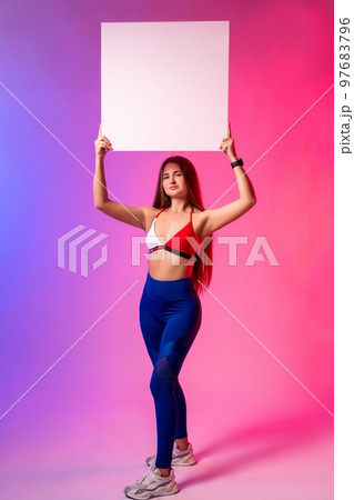 Confident young sportswoman showing empty banner in bright studio Confident young sportswoman showing empty banner in bright studio 97683796