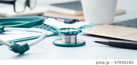 Green medical stethoscope closeup on doctor desk with pen and laptop 97690280