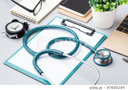 Doctor desk with green medical stethoscope on clipboard and laptop 97690284