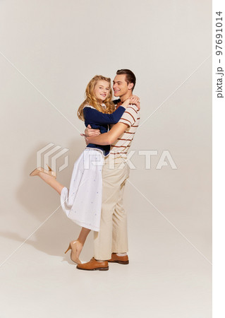 Emotional young, beautiful, stylish couple in vintage style fashion clothes hugging isolated over light background. 60s, 70s american culture concept 97691014