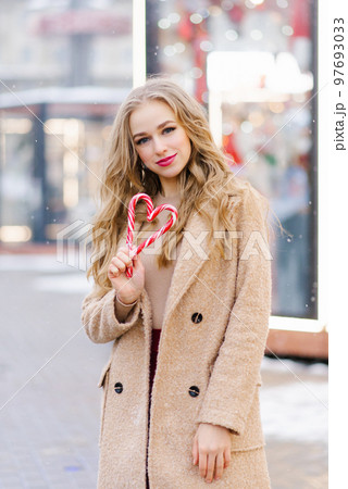 A happy smiling lady poses at a street holiday fair, holding lollipops in her hands. A funny girl makes a heart out of lollipops on a stick. The concept of Christmas or Valentine's Day A happy smiling lady poses at a street holiday fair, holding lollipops in her hands. A funny girl makes a heart out of lollipops on a stick. The concept of Christmas or Valentine's Day 97693033