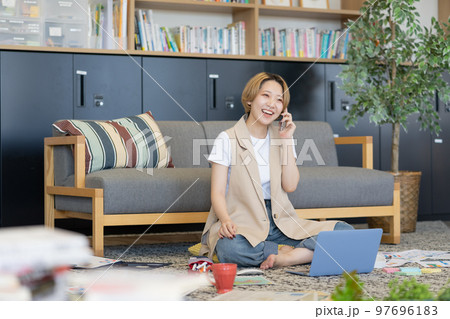床に書類を広げてスマホで会話する若い女性 97696183