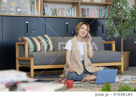 床に書類を広げてスマホで会話する若い女性 97696184
