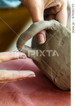 Women's hands knead the clay and sculpt a cup or bowl from it. The process of manufacturing a ceramic product,close up 97696745