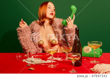 Portrait of beautiful redhead girl in pink fur coat sitting at the table with champagne over green background. Merry Christmas. Portrait of beautiful redhead girl in pink fur coat sitting at the table with champagne over green background. Merry Christmas. 97697342