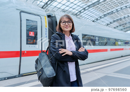 Woman passenger on railway platform inside station, with crossed arms looking at camera Woman passenger on railway platform inside station, with crossed arms looking at camera 97698560
