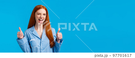 You go girl, women power. Encouraged and optimistic good-looking redhead woman in nightwear assure everything awesome, promote great product, show thumbs-up in like or approval, wink 97701617